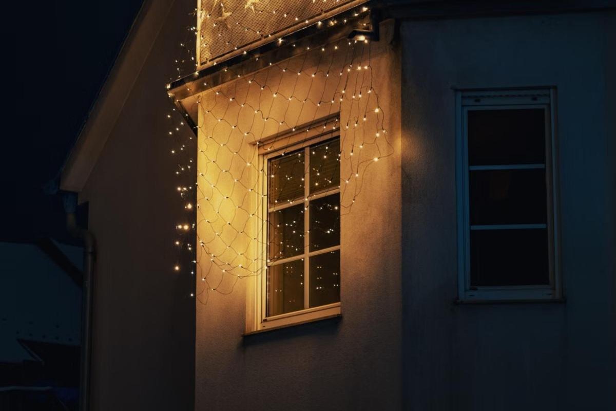 Ventana y balcón de una casa cubiertos con luces cálidas de navidad